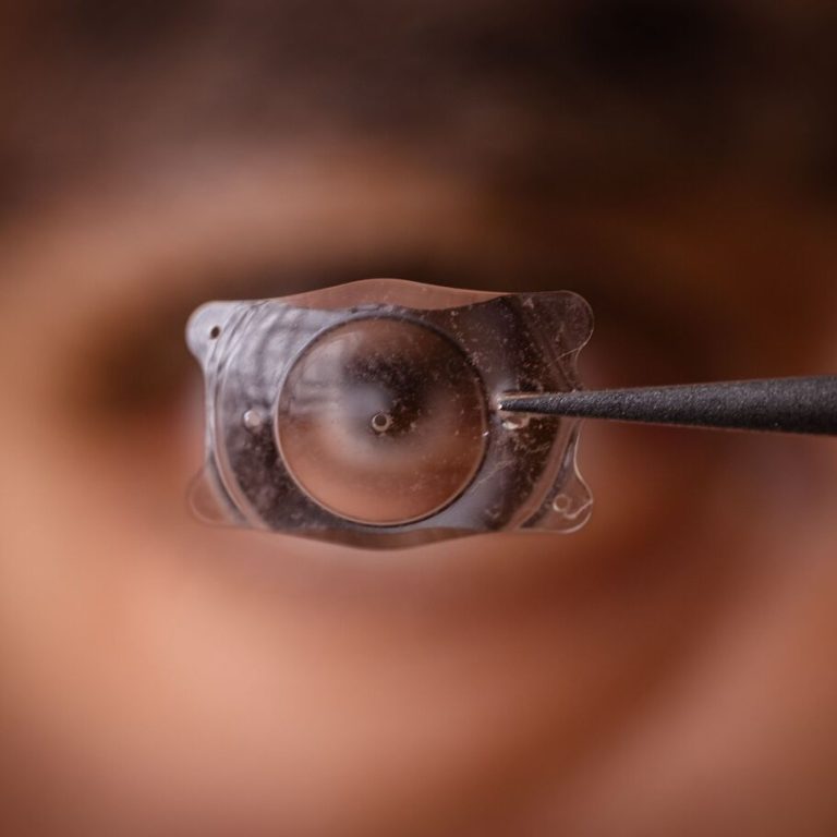Close-up of a person holding a contact lens with a tweezer, focusing on the lens.